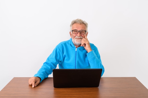 homem barbudo sênior feliz sorrindo enquanto está sentado com o laptop na mesa de madeira em branco