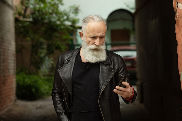 Homem barbudo sênior mensagens de texto no telefone. Empresário profissional urbano casual usando smartphone fora