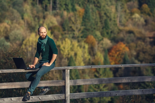 Homem barbudo senta-se no terraço e trabalhando no conceito de laptop de trabalho remoto na Internet