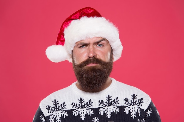 homem barbudo sério chapéu de Papai Noel brutal hipster suéter favorito fundo vermelho férias de inverno diversão rosto sério bigode retrato de homem de Papai Noel com barba festa de ano novo véspera de Natal