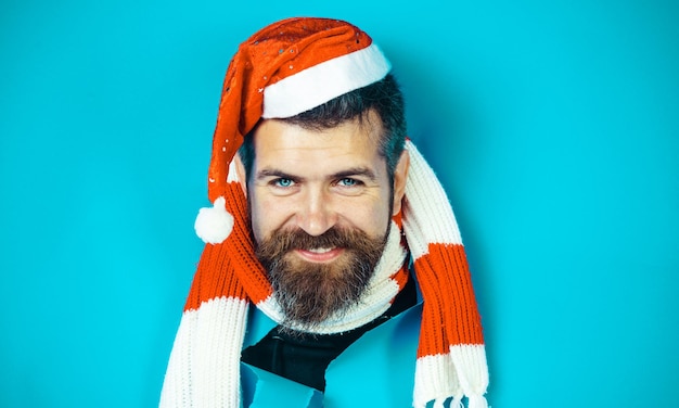 Homem barbudo sorridente com chapéu de papai noel e cachecol listrado olhando através das vendas de natal de buraco de papel