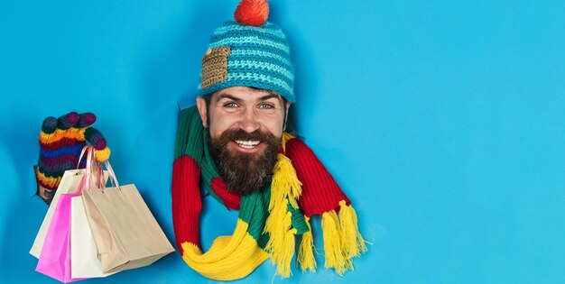 Foto homem barbudo sorridente em roupas de inverno com sacos de compras olhando através de um buraco de papel homem bonito em