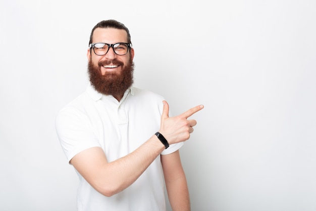 Homem barbudo sorridente está apontando de lado no fundo branco.