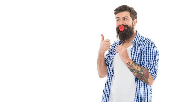 Homem barbudo sorridente feliz tirando sarro com adereços de festa para os lábios photobooth dando polegares para cima