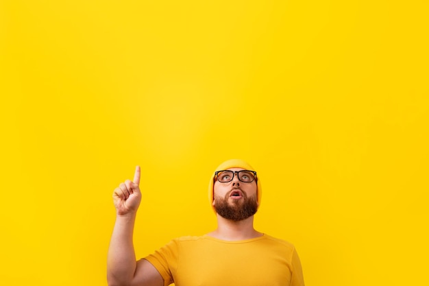 Homem barbudo surpreso com o dedo para cima, olhando sobre fundo amarelo, conceito de publicidade