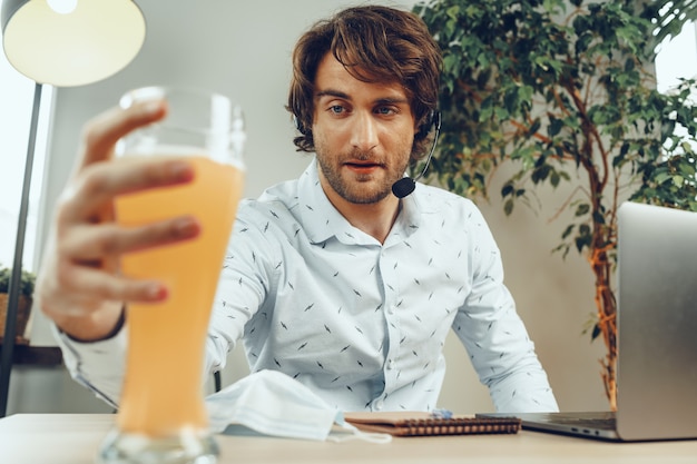 Homem barbudo usando seu laptop enquanto bebe um copo de cerveja sentado à mesa