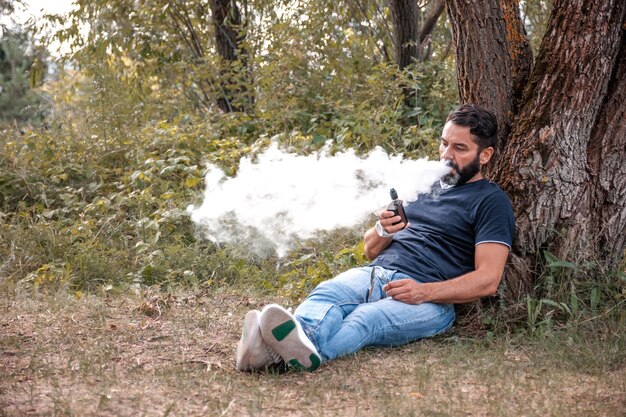 Homem Beardedvape fumando um cigarro eletrônico na natureza. Maneiras modernas de parar de fumar.