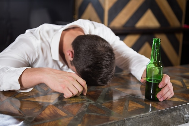 Homem bêbado deitado em um balcão com garrafa de cerveja