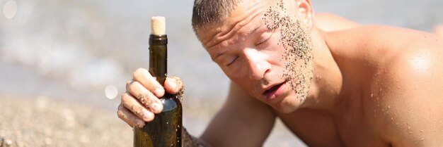 Homem bêbado na praia com os olhos fechados segurando uma garrafa de vinho e bebendo álcool no calor na praia