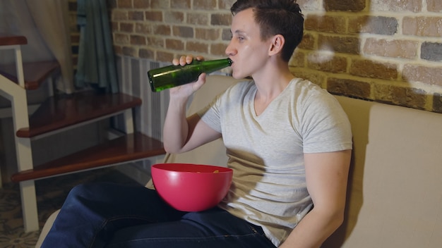 Homem bebe cerveja e batatas fritas na frente da tv.