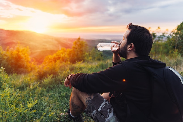 Homem bebendo água e apreciando o pôr do sol da montanha