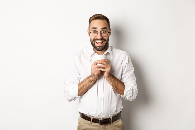 Homem bebendo café e parecendo animado, desfrutando da bebida, em pé sobre um fundo branco.