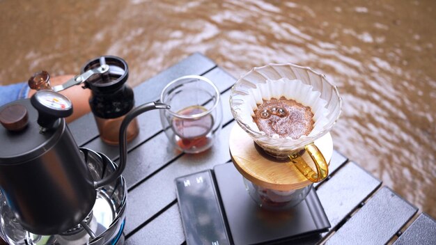 Homem bebendo café quente e acampando perto do rio no parque natural. Atividade ao ar livre e relaxamento nas férias.