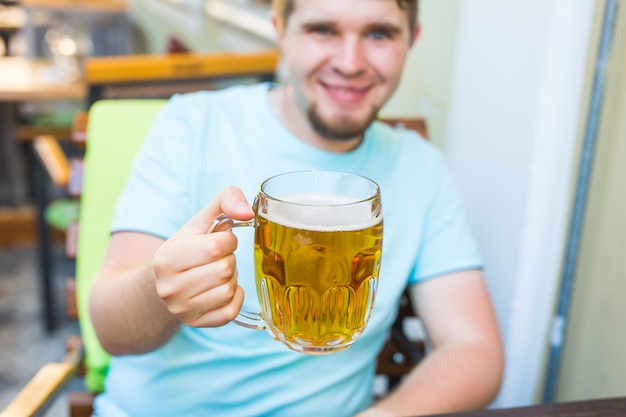 Homem bebendo cerveja. Jovem bonito bebendo cerveja enquanto está sentado no bar ao ar livre