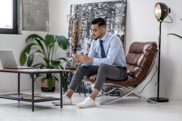 Homem bem sucedido sentado na cadeira olhando para smartphone