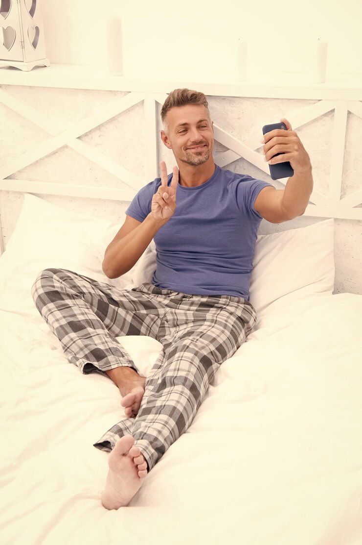 Foto homem blogueiro com telefone usar pijama gestando homem blogueiros com telefone na cama foto de homem blogueira com telefone em casa blogueiro homem com telefone no quarto