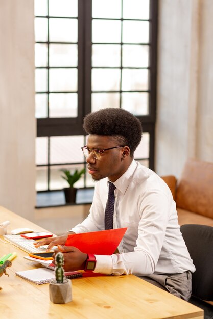 Homem bom e inteligente sentado na mesa do escritório enquanto faz seu trabalho