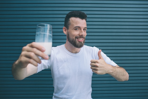 Homem bom e positivo está segurando o copo de mils e aparecendo o polegar grande. ele gosta disso. cara está olhando na câmera e sorrindo. isolado em listrado