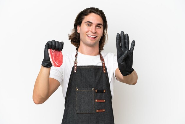 Homem bonito açougueiro vestindo um avental e servindo carne fresca isolada no fundo branco feliz e contando quatro com os dedos