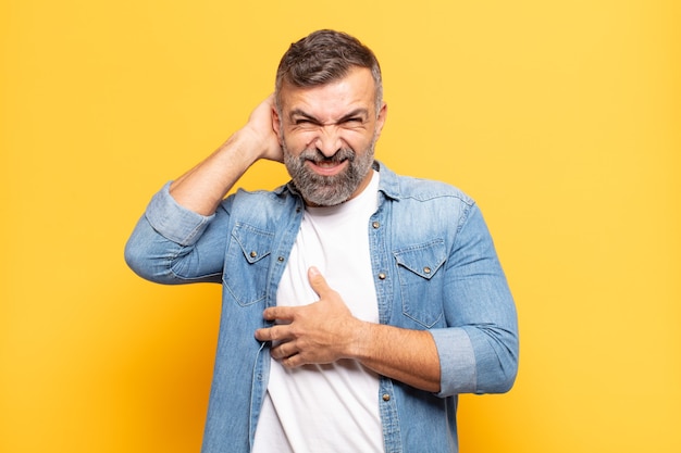 Homem bonito adulto se sentindo estressado, frustrado e cansado, esfregando o pescoço dolorido, com uma aparência preocupada e preocupada