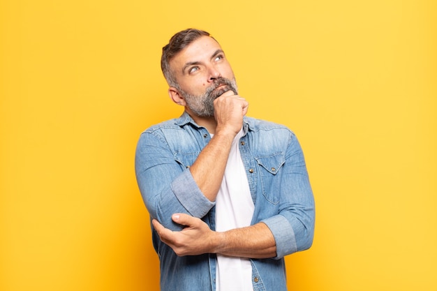 Homem bonito adulto se sentindo pensativo, imaginando ou imaginando ideias, sonhando acordado e olhando para cima para copiar o espaço