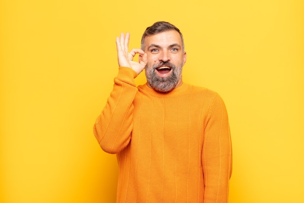 Homem bonito adulto sentindo-se bem-sucedido e satisfeito, sorrindo com a boca bem aberta, fazendo sinal de ok com a mão