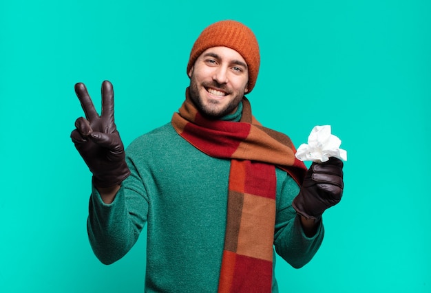 Homem bonito adulto sorrindo e parecendo feliz, despreocupado e positivo, gesticulando vitória ou paz com uma mão. conceito de doença e frio