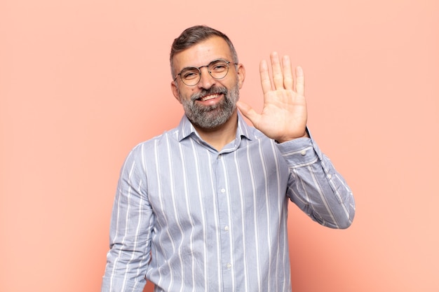 Homem bonito adulto sorrindo feliz e alegre, acenando com a mão, dando as boas-vindas e cumprimentando você ou dizendo adeus