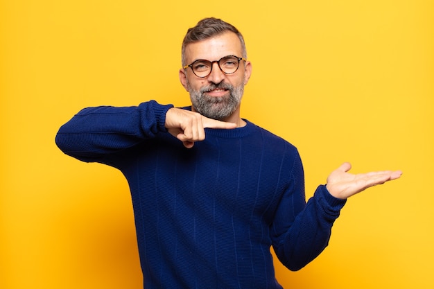 Homem bonito adulto sorrindo, sentindo-se feliz, despreocupado e satisfeito, apontando para um conceito ou ideia no espaço da cópia ao lado