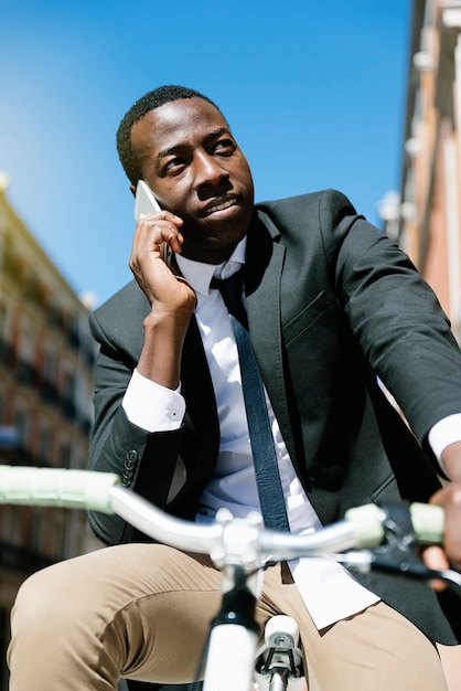 Homem bonito africano com telefone celular e bicicleta de engrenagem fixa na rua.