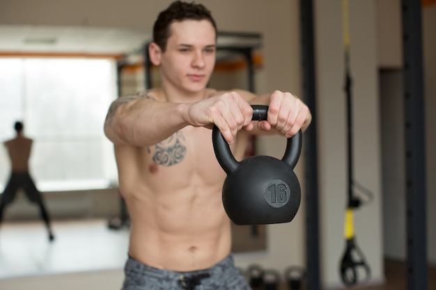 Homem bonito agachado com kettlebell na academia