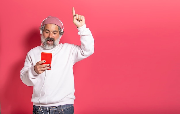 Homem bonito alegre e sorridente ouvindo streaming de música com fones de ouvido isolados no fundo do estúdio rosa com espaço para texto