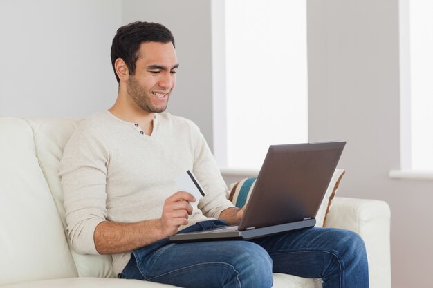 Foto homem bonito alegre usando seu cartão de crédito para comprar on-line