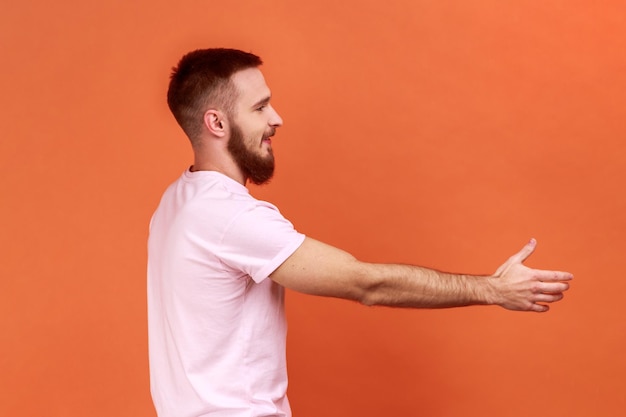 Homem bonito amigável positivo, estendendo a mão para o lado, dando um aperto de mão