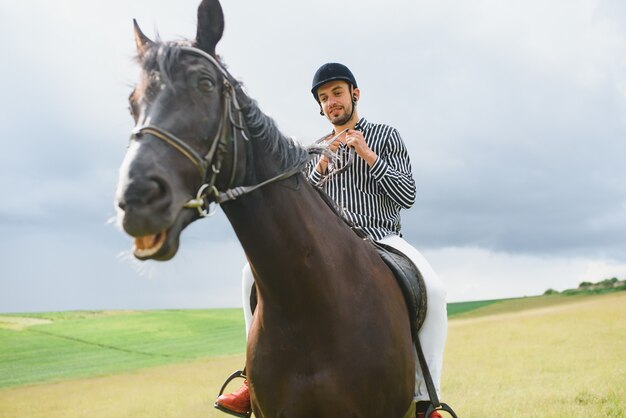 Homem bonito andando a cavalo no campo no verão