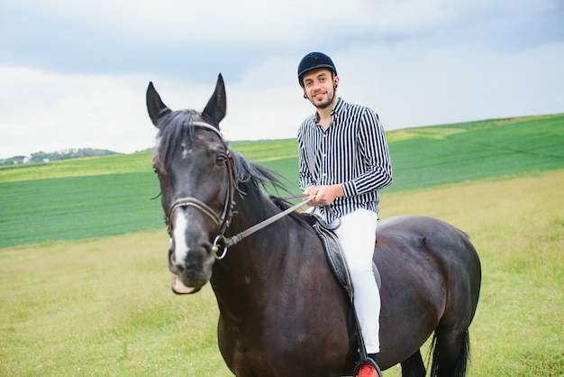 Homem bonito andando a cavalo no campo no verão