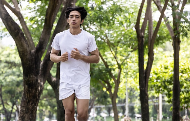 Homem bonito asiático de camisa branca correndo no parque Conceito para estilo de vida saudável no parque