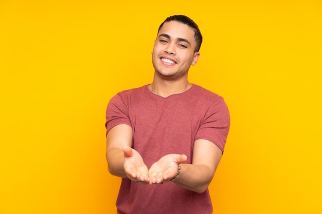 Homem bonito asiático isolado em fundo amarelo mantém as palmas unidas. Pessoa pede algo