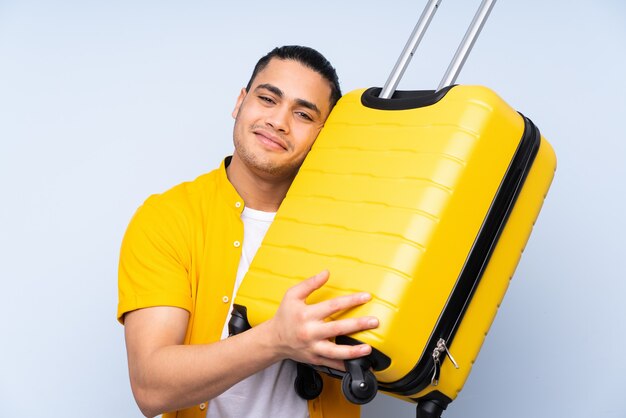 Homem bonito asiático isolado em um fundo azul de férias com mala de viagem