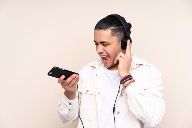 Homem bonito asiático isolado em uma parede bege ouvindo música com um celular e cantando