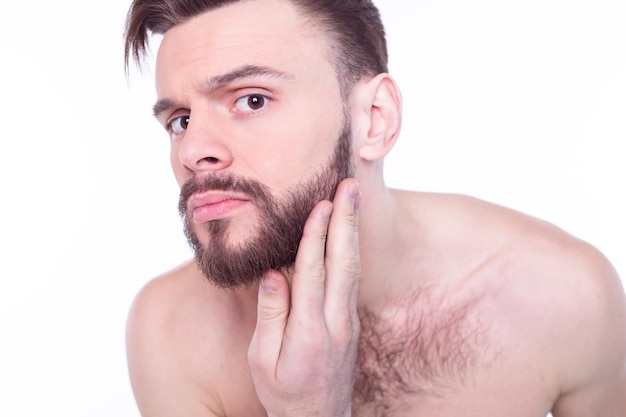 Homem bonito, atraente, brutal, moderno, viril, confiante, nu, tocando sua pele de rosto ideal perfeita, olhando para a câmera e posando isolado no fundo branco após o banho