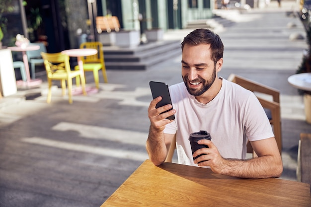 Foto homem bonito bebendo café e olhando para um smartphone no café