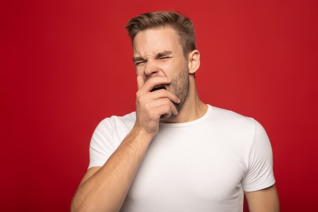 homem bonito, bocejando com os olhos fechados, isolados no vermelho