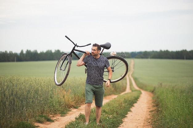 Homem bonito carrega sua bicicleta a pé ao longo de uma estrada de campo