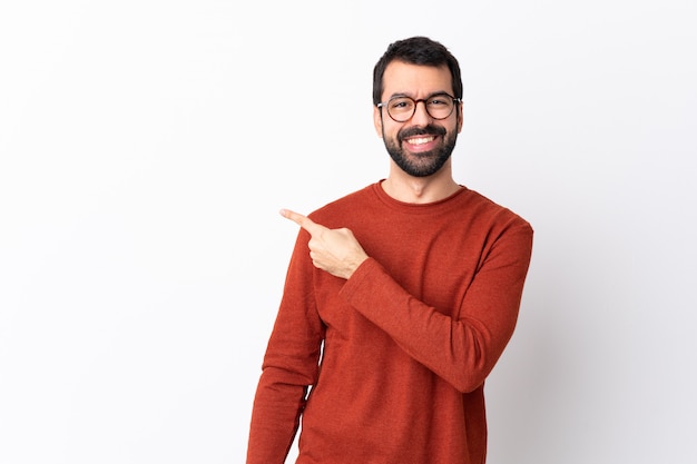 Foto homem bonito caucasiano com barba sobre parede branca isolada, apontando para o lado para apresentar um produto