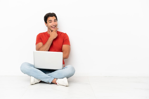 Homem bonito caucasiano com um laptop sentado no chão sorrindo