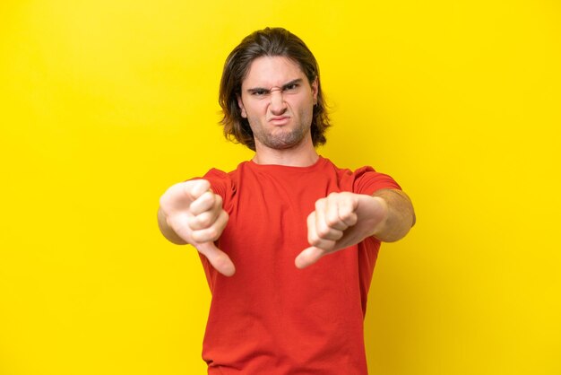 Homem bonito caucasiano isolado em fundo amarelo, mostrando o polegar para baixo com as duas mãos
