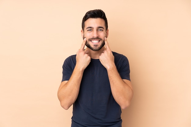 Homem bonito caucasiano isolado em uma parede bege sorrindo com uma expressão feliz e agradável