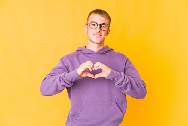 Homem bonito caucasiano jovem sorrindo e mostrando uma forma de coração com as mãos.