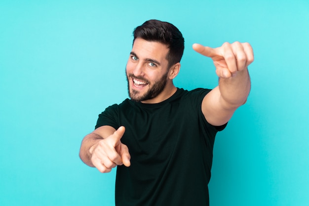 Homem bonito caucasiano na parede azul aponta o dedo para você enquanto sorrindo